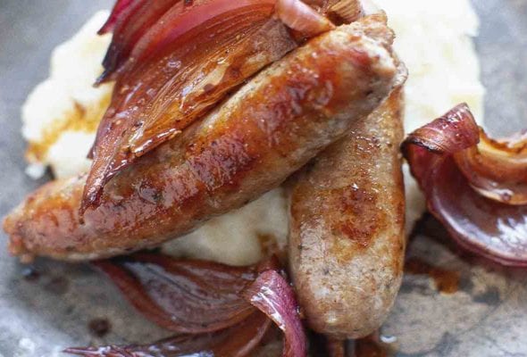 Two bangers and mash with cooked red onion in a bowl.