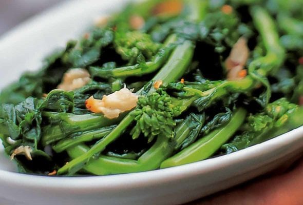 A white platter filled with broccoli rabe, topped with roasted garlic and red pepper flakes.
