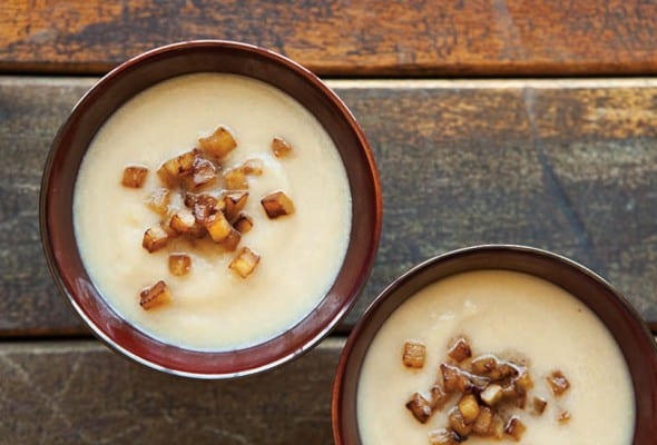 Two bowls of celery root soup with caramelized onions on a wooden table.