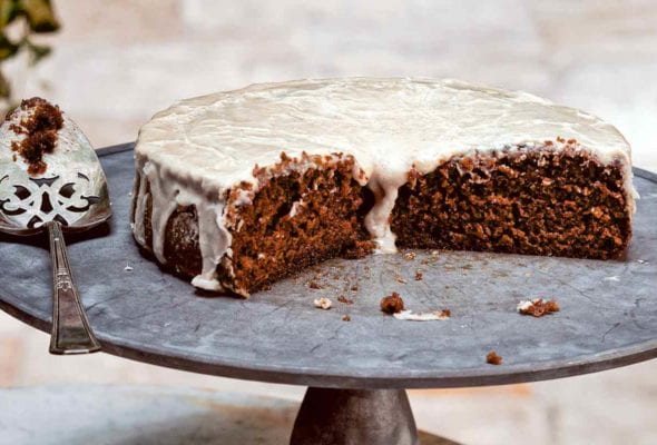 A cut root beer cake on a pewter platter with a slice on a decorative plate in front.