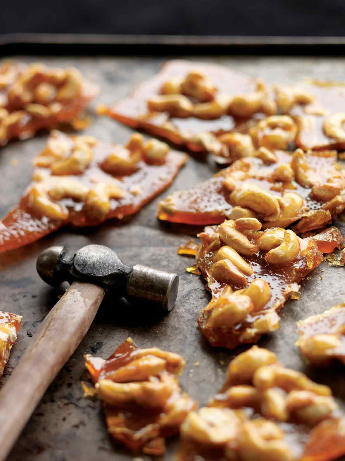 Pieces of broken cashew brittle with a hammer lying beside them.