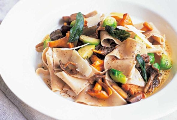 A white bowl filled with chestnut pasta, wild mushrooms, and Brussels sprouts.