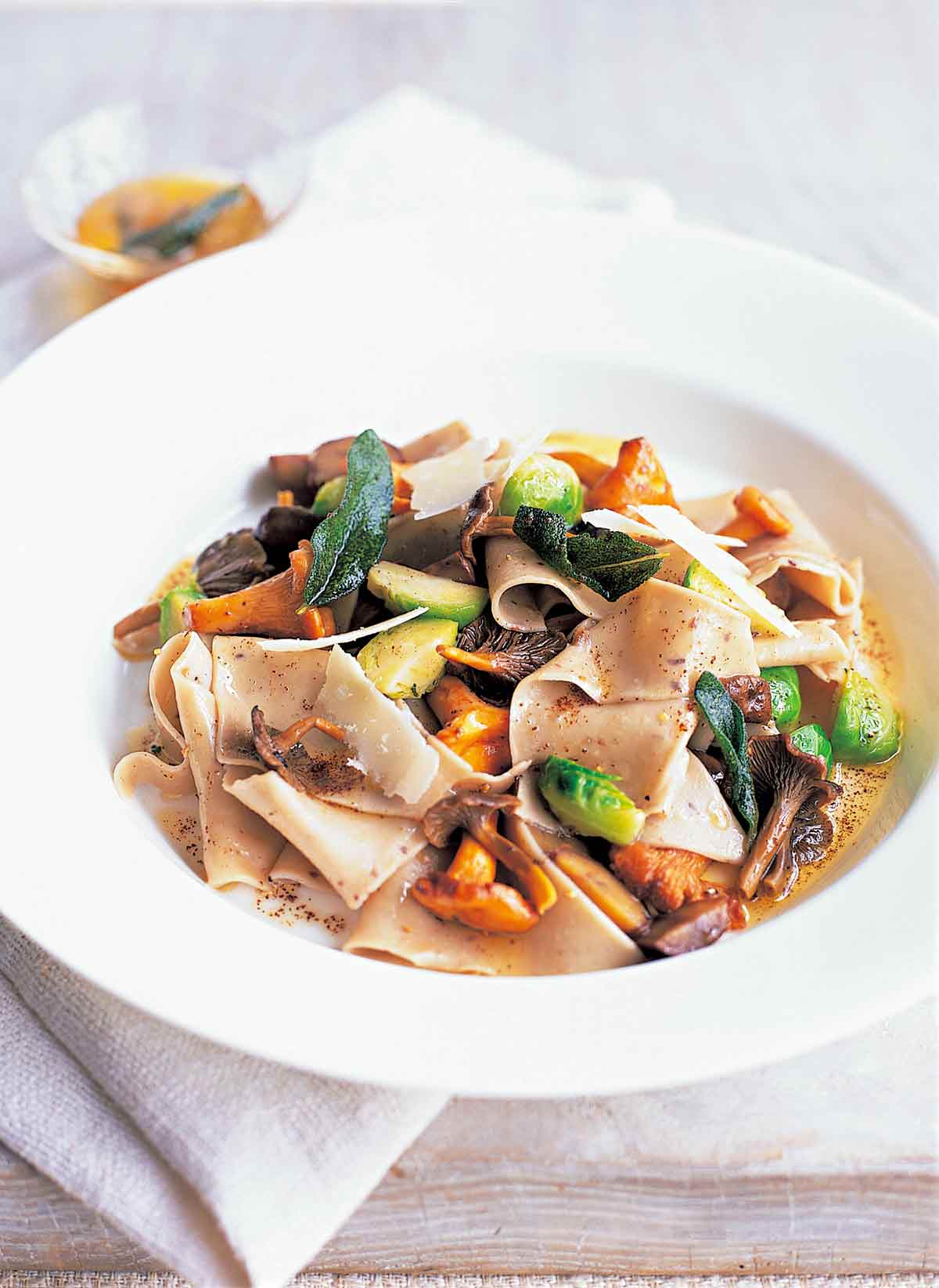A white bowl filled with chestnut pasta, wild mushrooms, and Brussels sprouts.