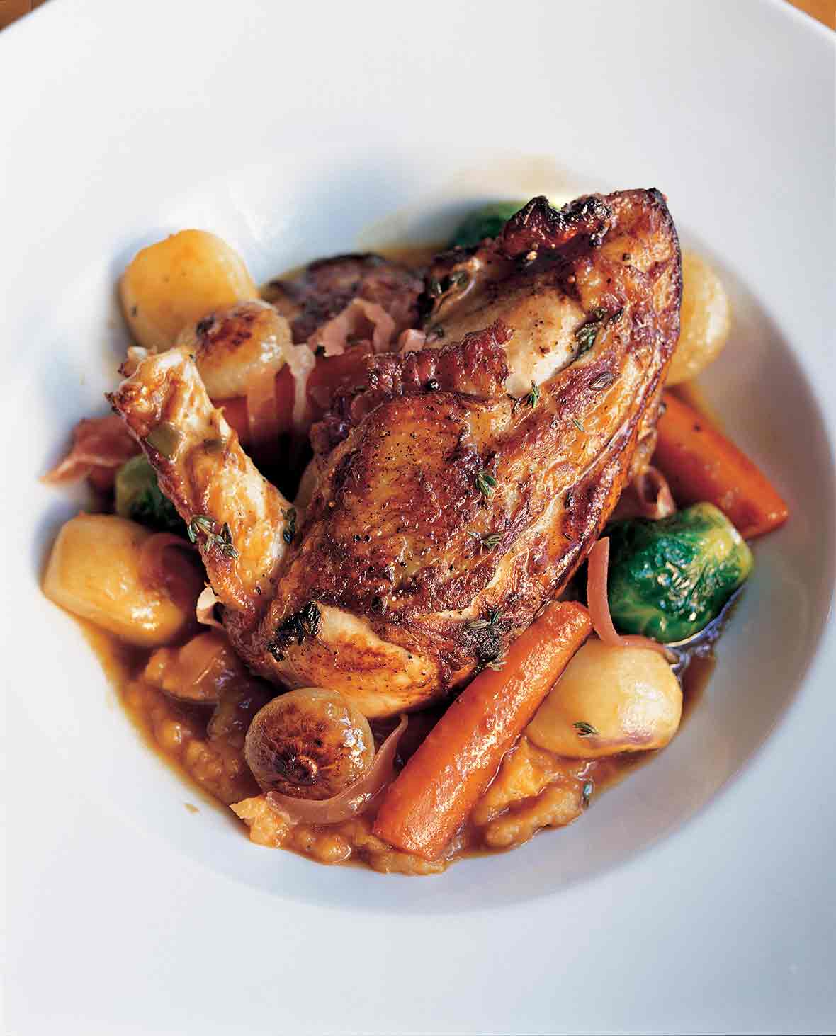 A large white serving bowl filled with chicken with autumn vegetables and Madeira wine.