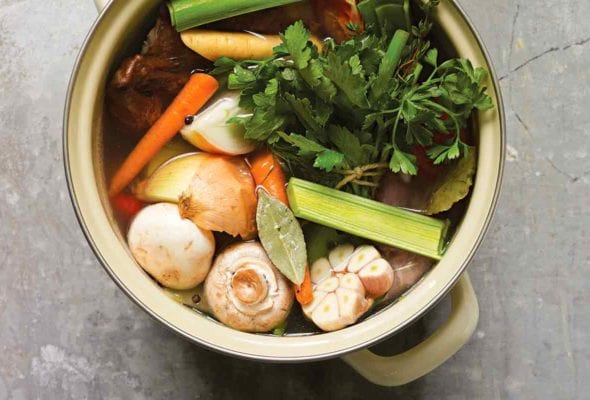 A stock pot filled with mushrooms, leeks, garlic, onion, carrots, and parsley for making roast chicken stock.