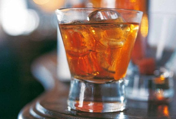 A highball glass filled with classic old-fashioned cocktail and large ice cubes.