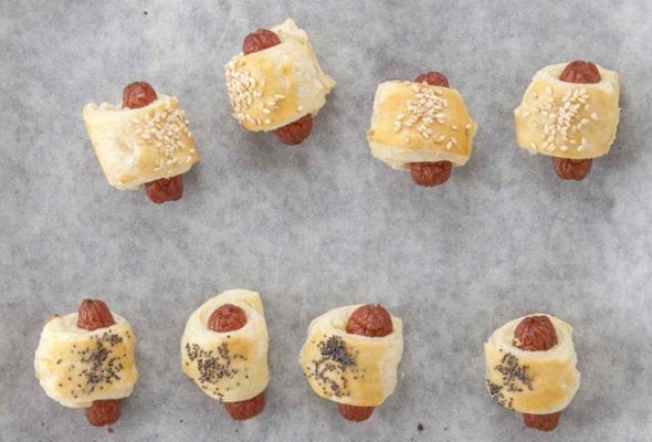 Eight mini hog dogs wrapped in puff pastry on a parchment lined baking sheet