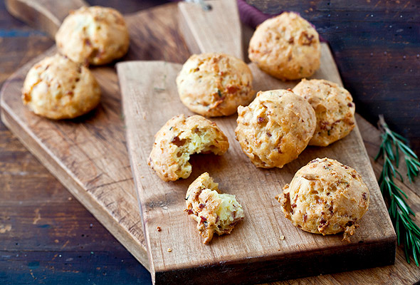 Prosciutto Grana Padano gougeres scattered on two wooden cutting boards with a sprig of rosemary alongside.