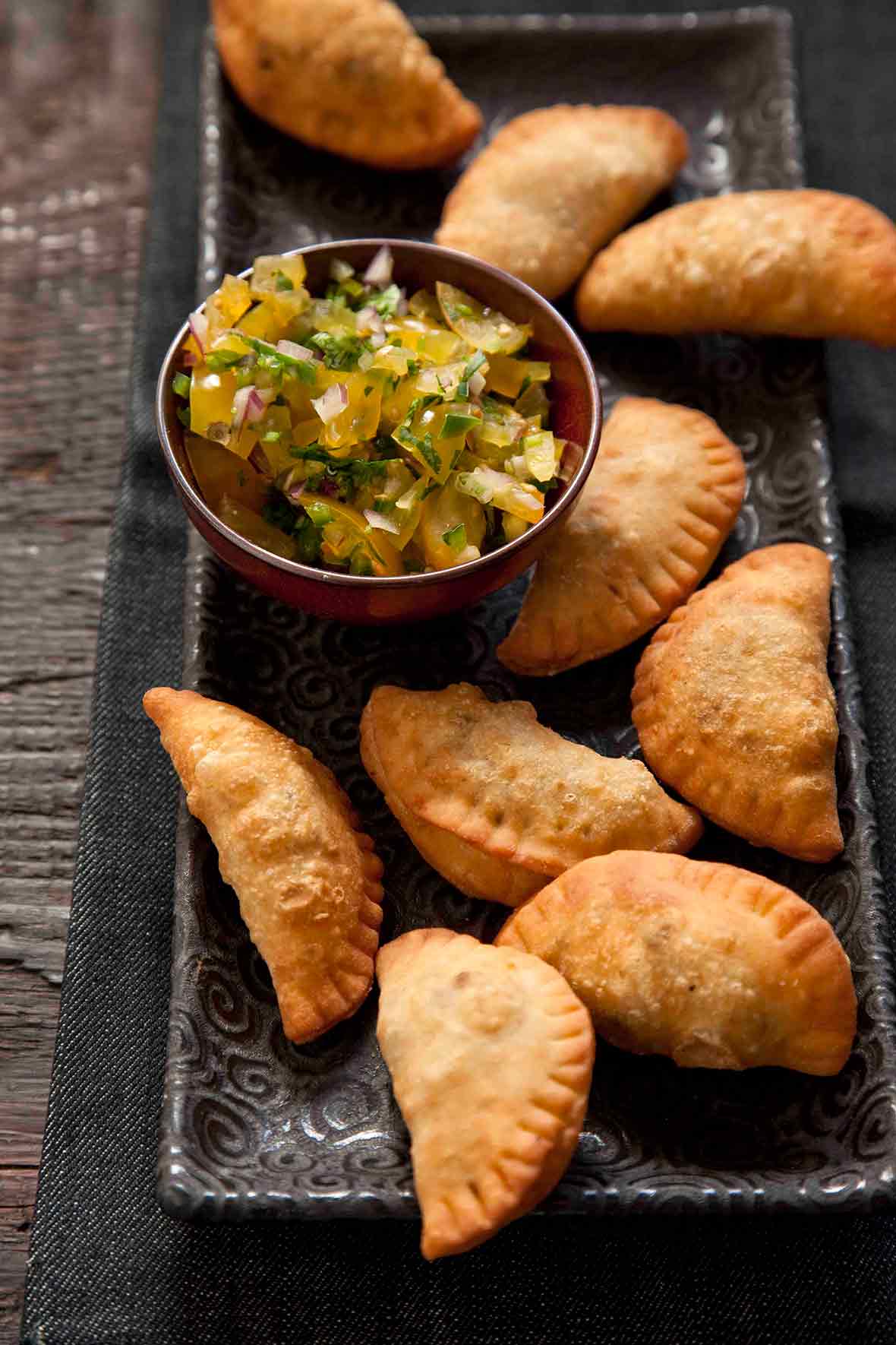 Platter of half-moon-shaped beef empanadas pastries, bowl of yellow salsa