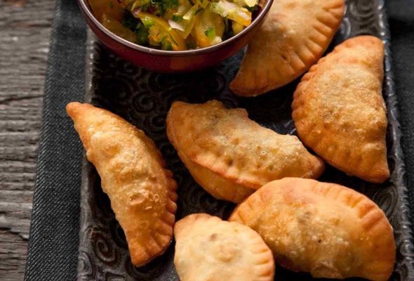 Platter of half-moon-shaped beef empanadas pastries, bowl of yellow salsa