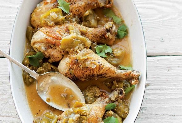 White oval dish with four chicken drumsticks, chopped green tomatillos, cilantro, onion, sliced chiles