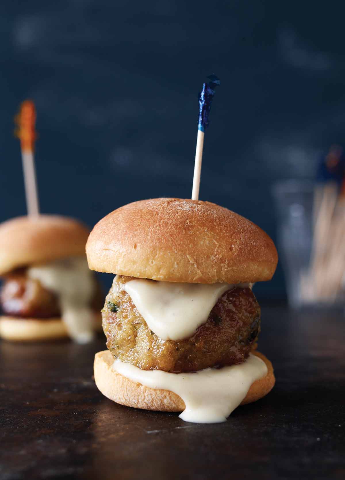 Two chicken meatball sliders with white sauce and toothpicks holding them together.