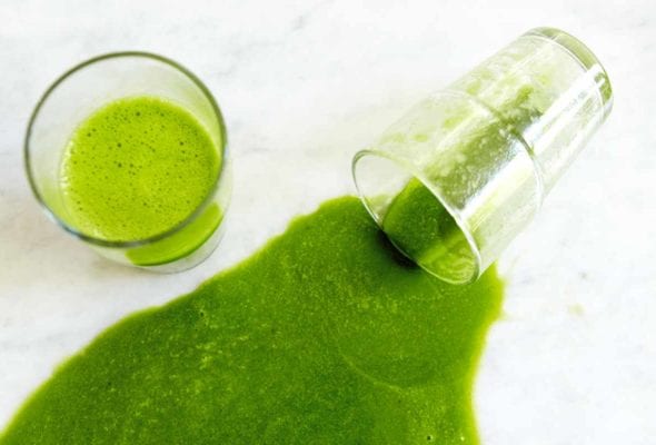 A glass of green smooth and a second glass that is on its side with green smoothie poured out.