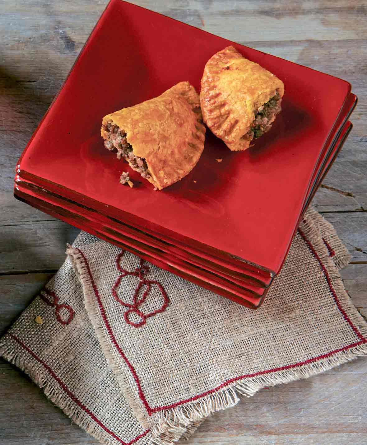 Pile of red square plates with a two halves of Jamaican beef turnovers, or empanadas