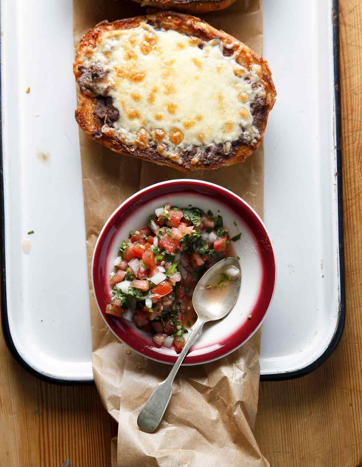 A white platter with two molletes and a bowl of pico de gallo.