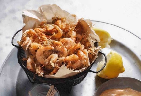 A basket of spiced shrimp with a bowl of paprika mayonnaise beside the shrimp, a halved lemon, and a cup of toothpicks.