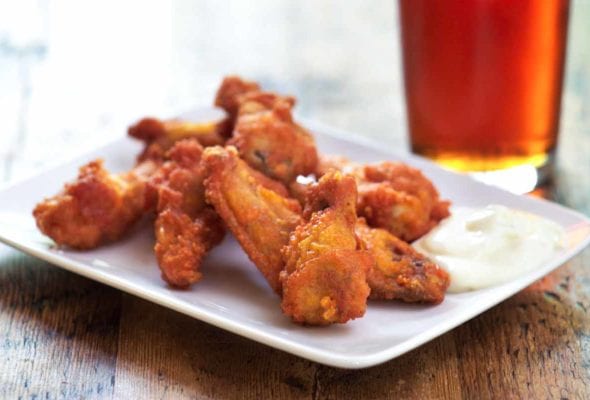 A pile of Tabasco chicken wings on a white plate with some ranch dip.