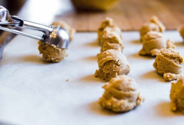 Rows of peanut butter sandies dough balls with a cookie scoop placing another dough ball on the surface.