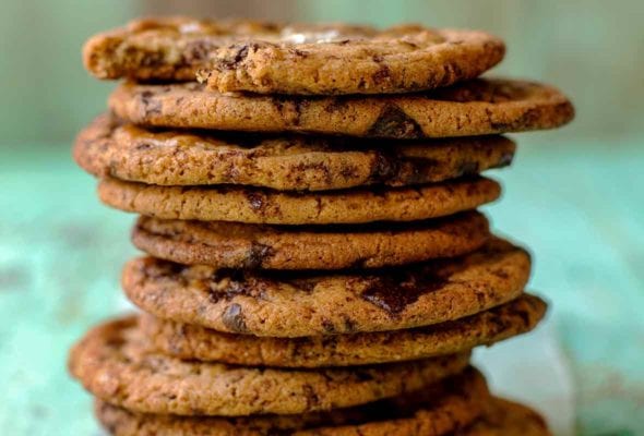 Stack of 10 chocolate chip cookies, each topped with sea salt on an aqua piece of wood