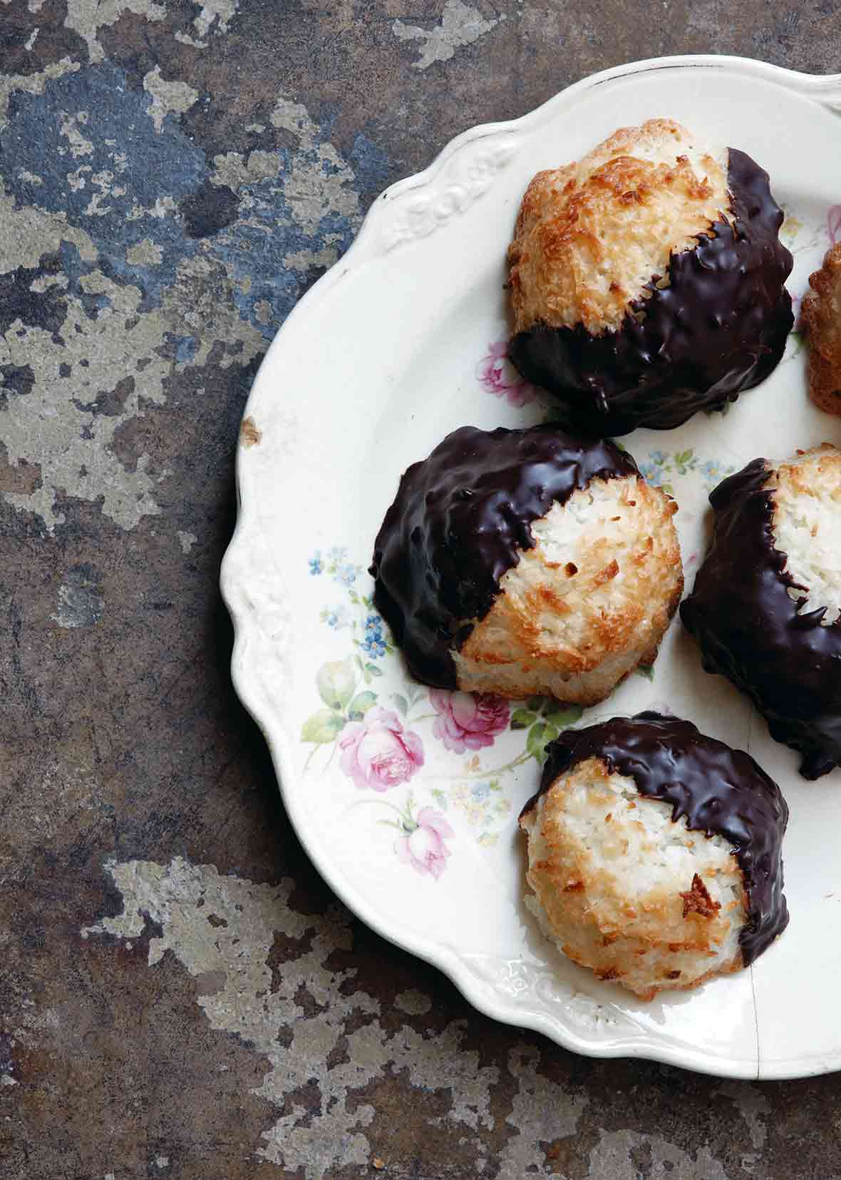 Five coconut macaroons dipped in chocolate arranged on a floral-patterned china plate.