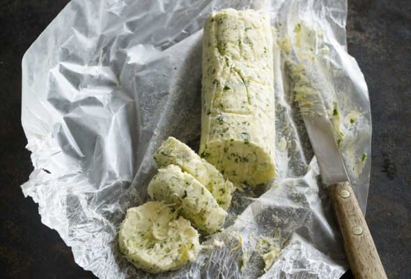 A log of lemon horseradish butter with a few rounds cut off on a piece of wax paper with a knife resting beside it.