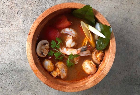 A wooden bowl filled with Tom Yum Goong soup, garnished with cilantro.