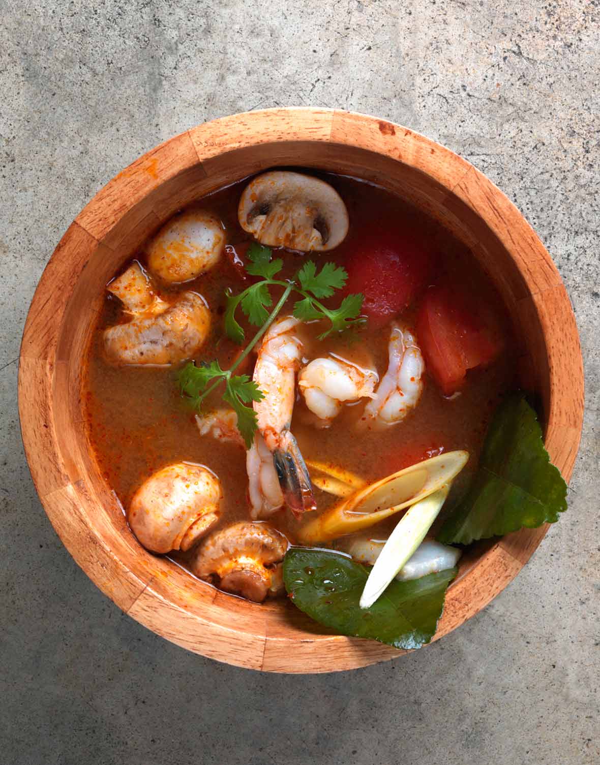 A wooden bowl filled with Tom Yum Goong soup, garnished with cilantro.