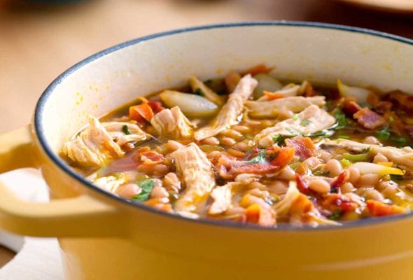 A yellow Dutch oven filled with white bean and chicken chili, topped with pieces of bacon.