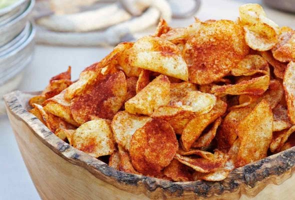 A carved wooden bowl filled with barbecue potato chips.