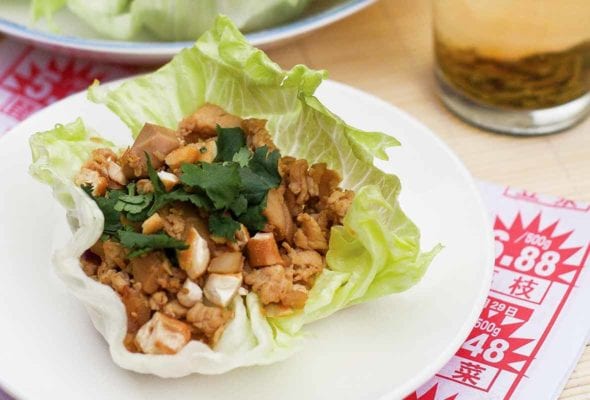A Chinese chicken lettuce cup topped with cashews and cilantro on a white plate.