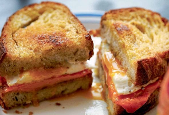 A fried egg sandwich cut in half on a white and blue plate with the knife resting in front.