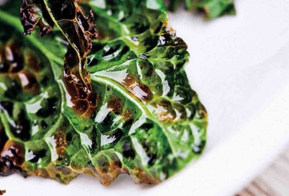 Leaves of grilled kale, coated with olive oil, on a white platter.