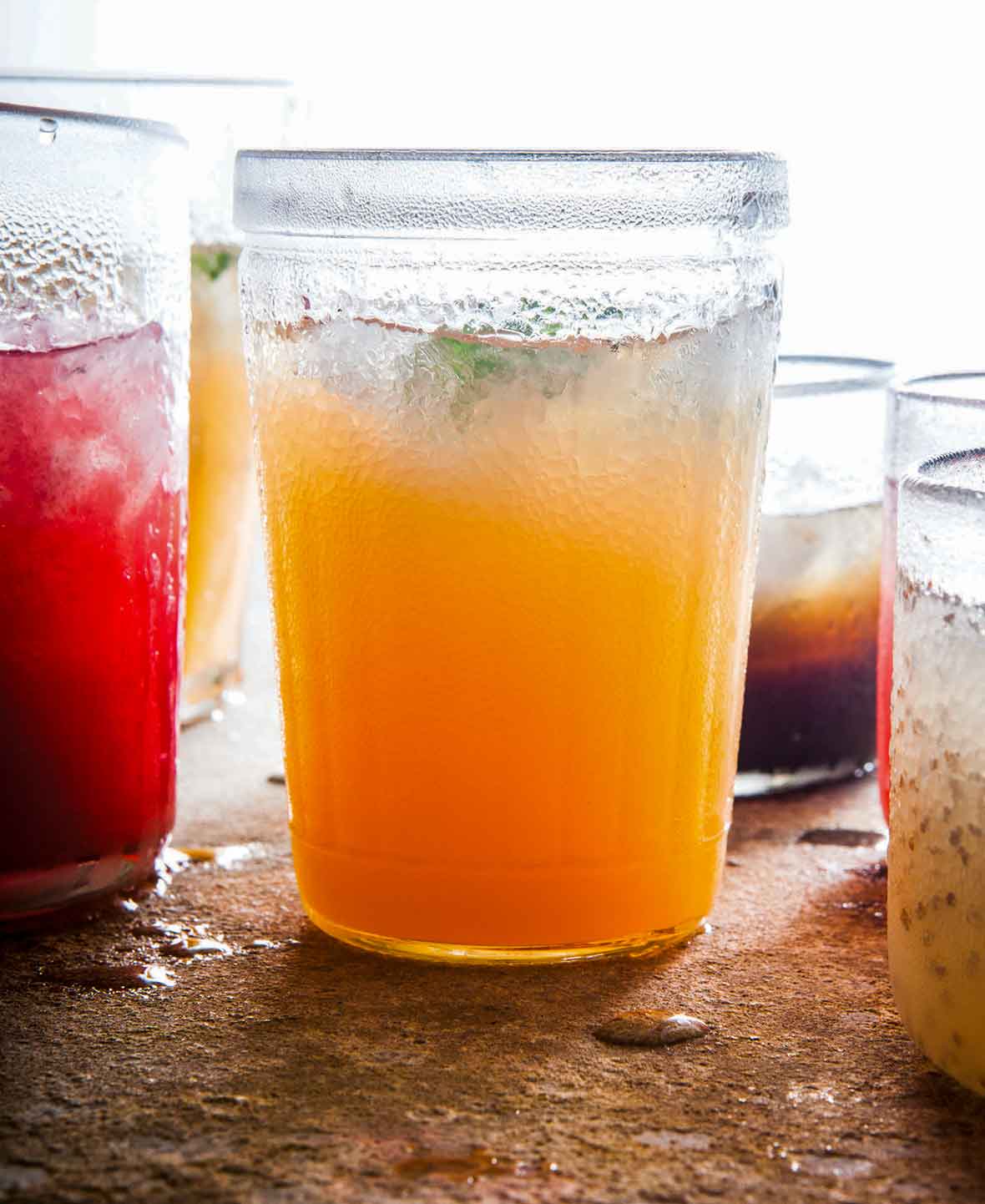 A glass filled with cantaloupe agua fresca, and glasses of other liquid around it.