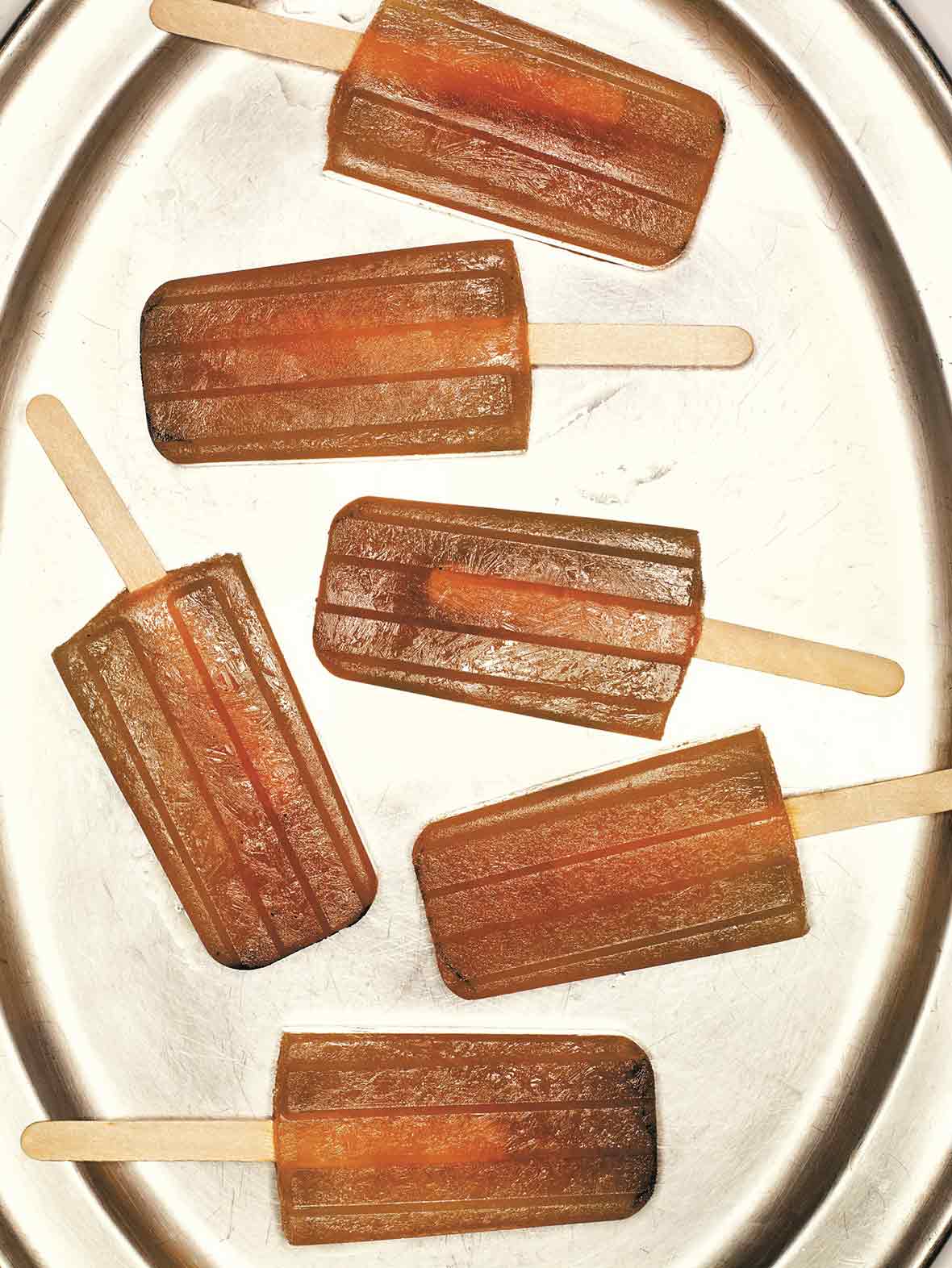 Six iced tea popsicles on a silver platter.