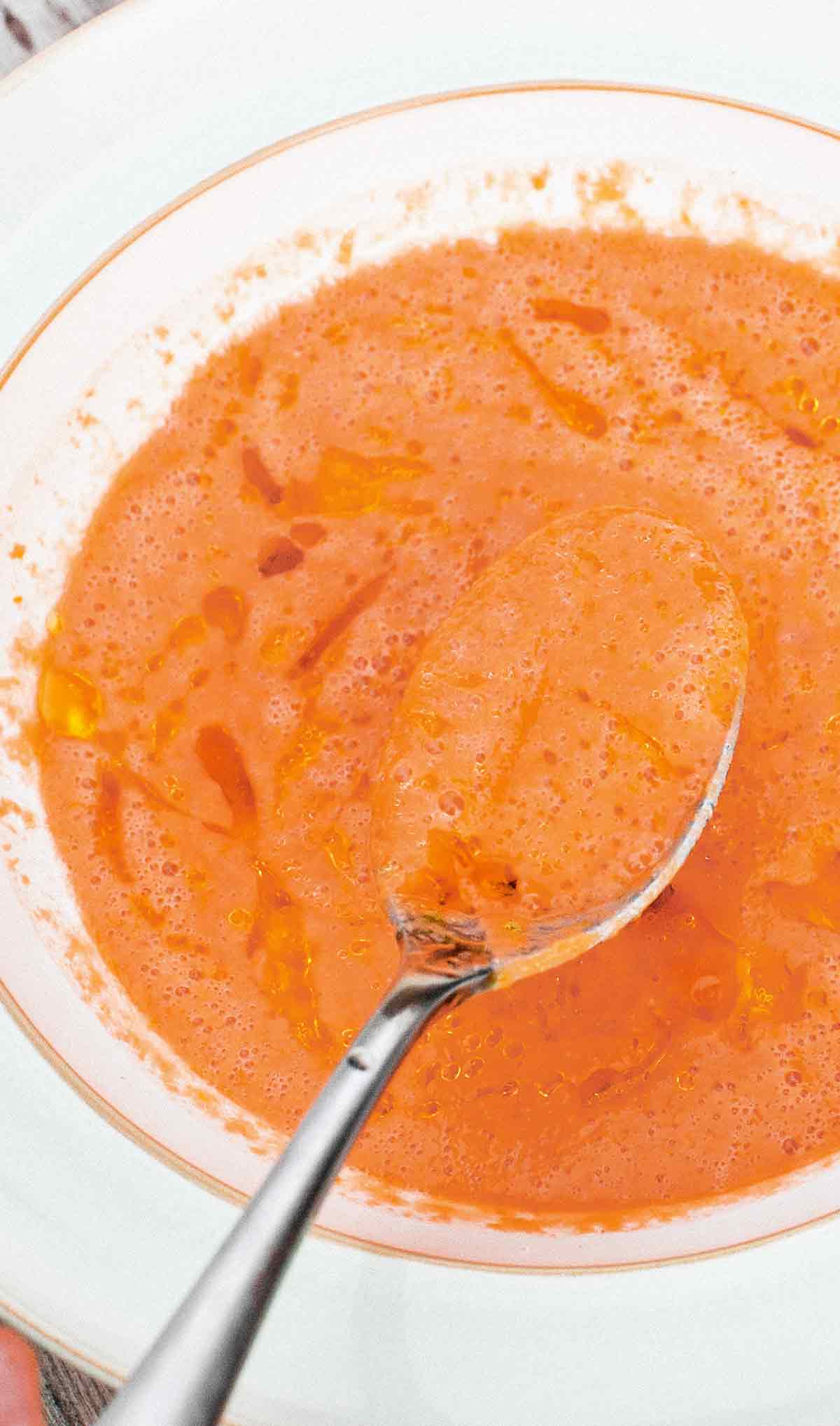 A white bowl filled with smoky gazpacho drizzled with extra-virgin olive oil, and a spoon resting inside the bowl.