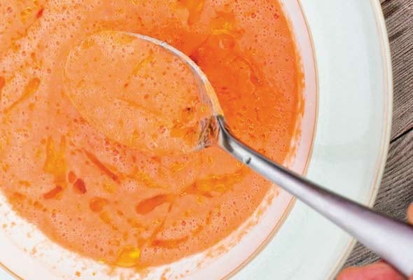 A white bowl filled with smoky gazpacho drizzled with extra-virgin olive oil, and a spoon resting inside the bowl.
