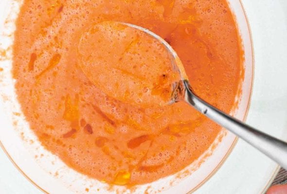A white bowl filled with smoky gazpacho drizzled with extra-virgin olive oil, and a spoon resting inside the bowl.