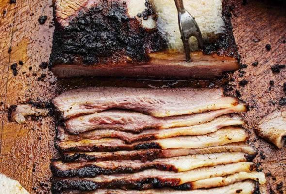 A slab of deeply smoked barbecue beef brisket being sliced on a cutting board