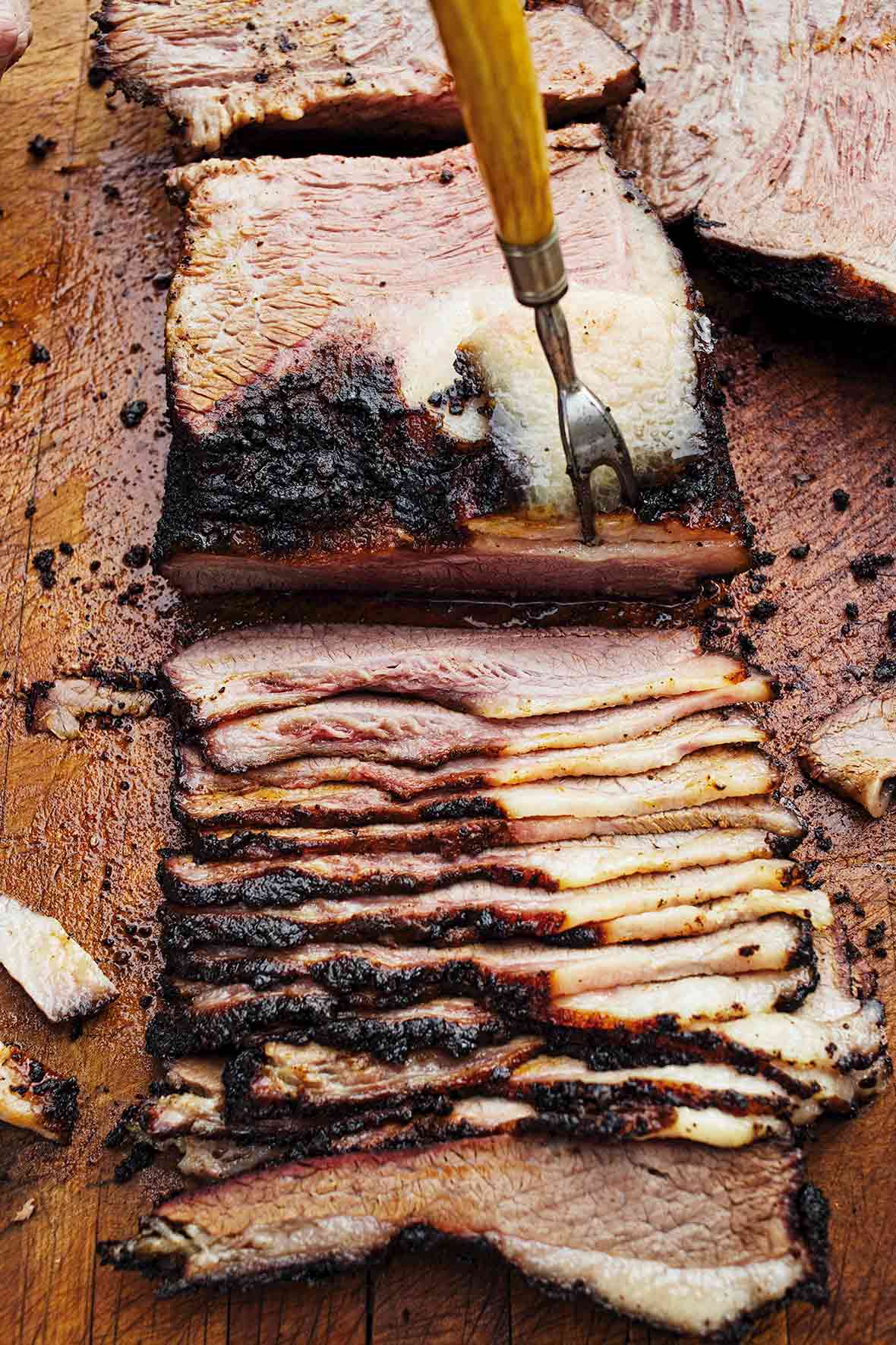 A slab of deeply smoked barbecue beef brisket being sliced on a cutting board