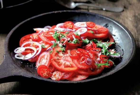 A wooden serving plate filled with sliced tomatoes, red onion, and chopped cilantro.