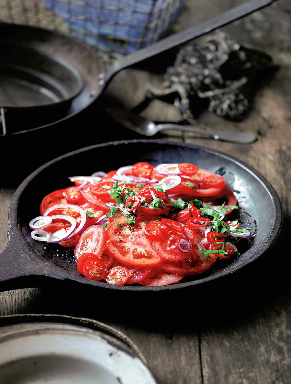 A wooden serving plate filled with sliced tomatoes, red onion, and chopped cilantro.