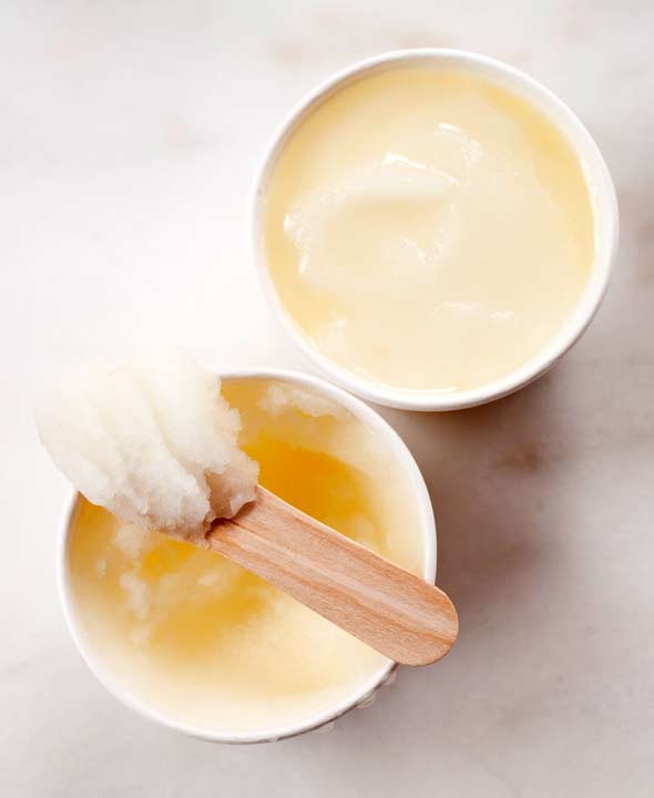 Two cardboard cups filled with lemon ice, one with a wooden spoon with of heap of ice on it