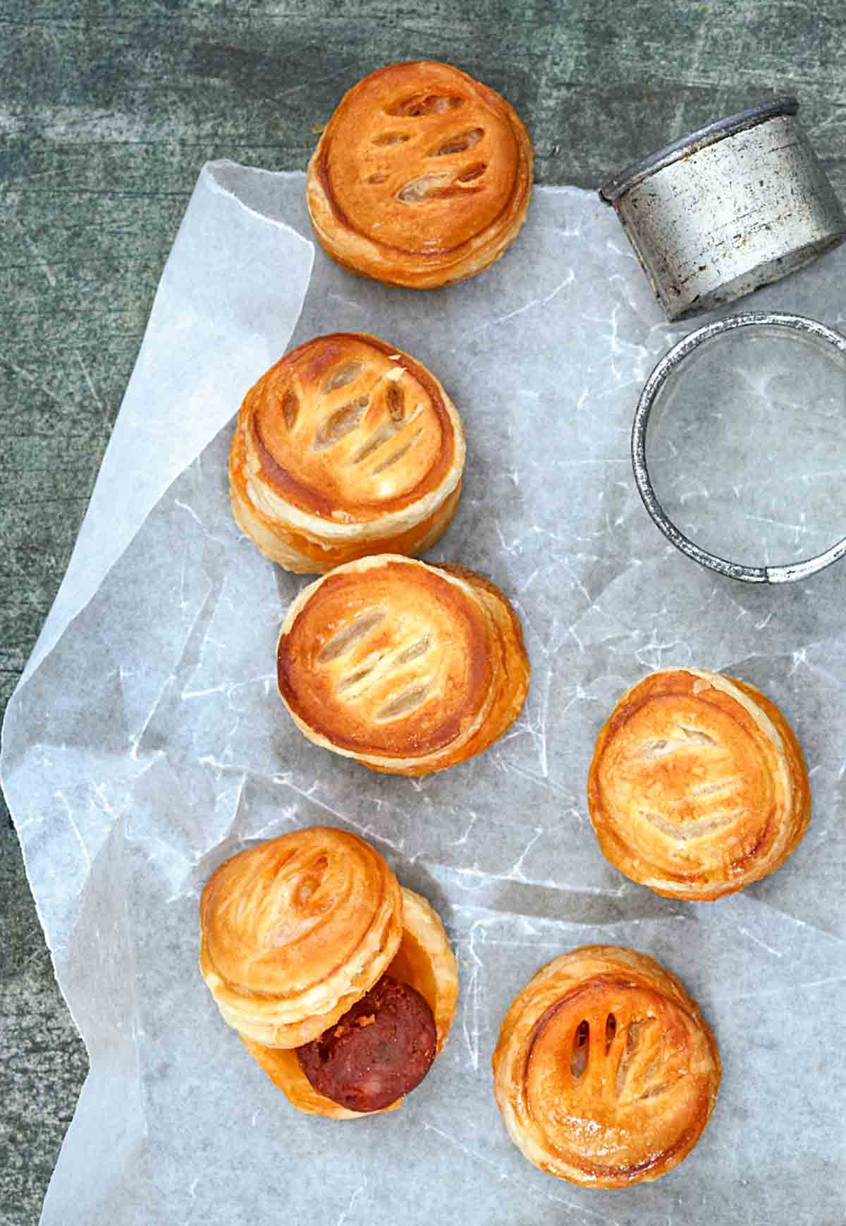 Several chorizo bites sandwich between puff pastry rounds and a biscuit cutter on a sheet of wax paper.