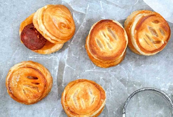 Several chorizo bites sandwich between puff pastry rounds and a biscuit cutter on a sheet of wax paper.