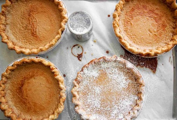 Four Hoosier sugar cream pies, one dusted with confectioners' sugar on a sheet of parchment.