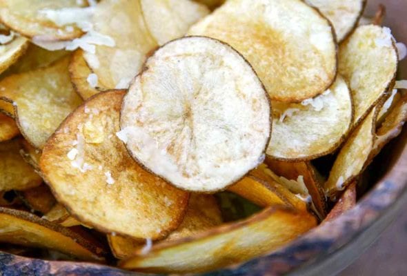 A wooden bowl filled with Manchego potato chips and sprinkled with more Manchego cheese.