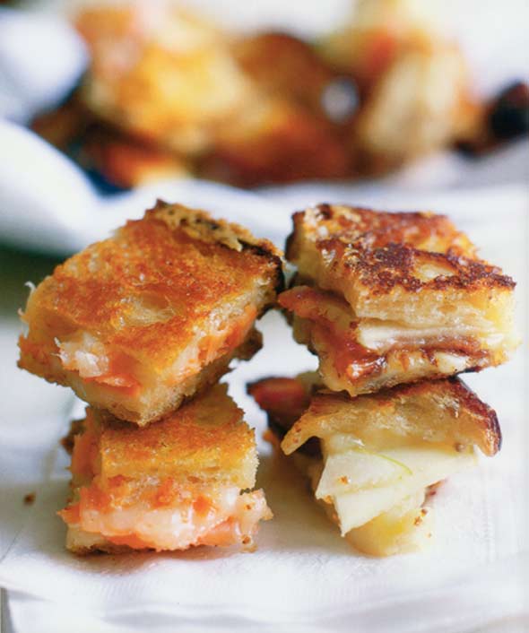 Four pieces of Cheddar, bacon, apple grilled cheese sandwiches stacked on top of each other.