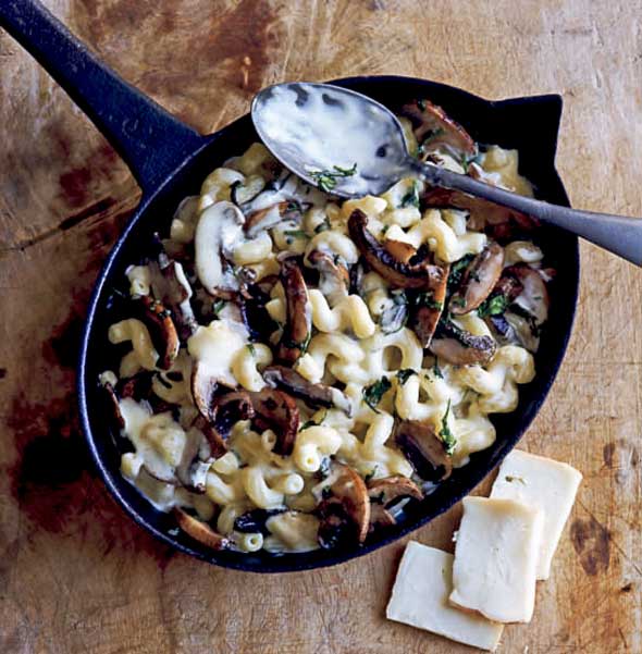 An oval skillet filled with mushroom macaroni and cheese with a spoon resting on top.