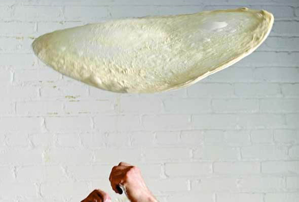 A thin circle of stretched pizza dough being tossed in the air.