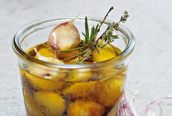 A pint-sized canning jar filled with garlic confit, sprigs of thyme and rosemary, and a partially separated head of garlic lying beside the jar.